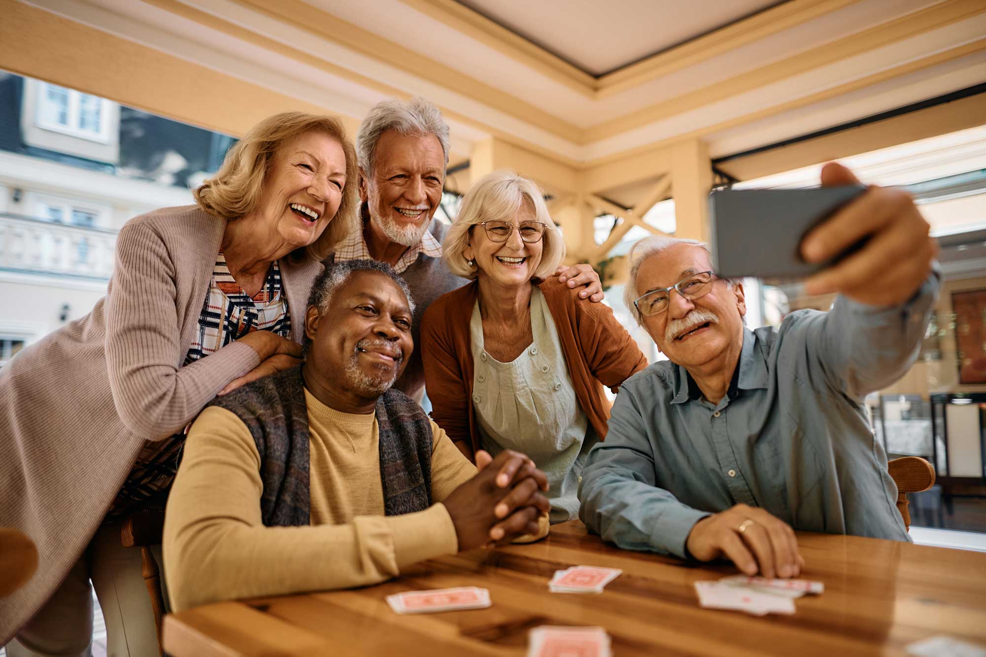 a group of senior friends gathered at home playing cards and posing for a selfie