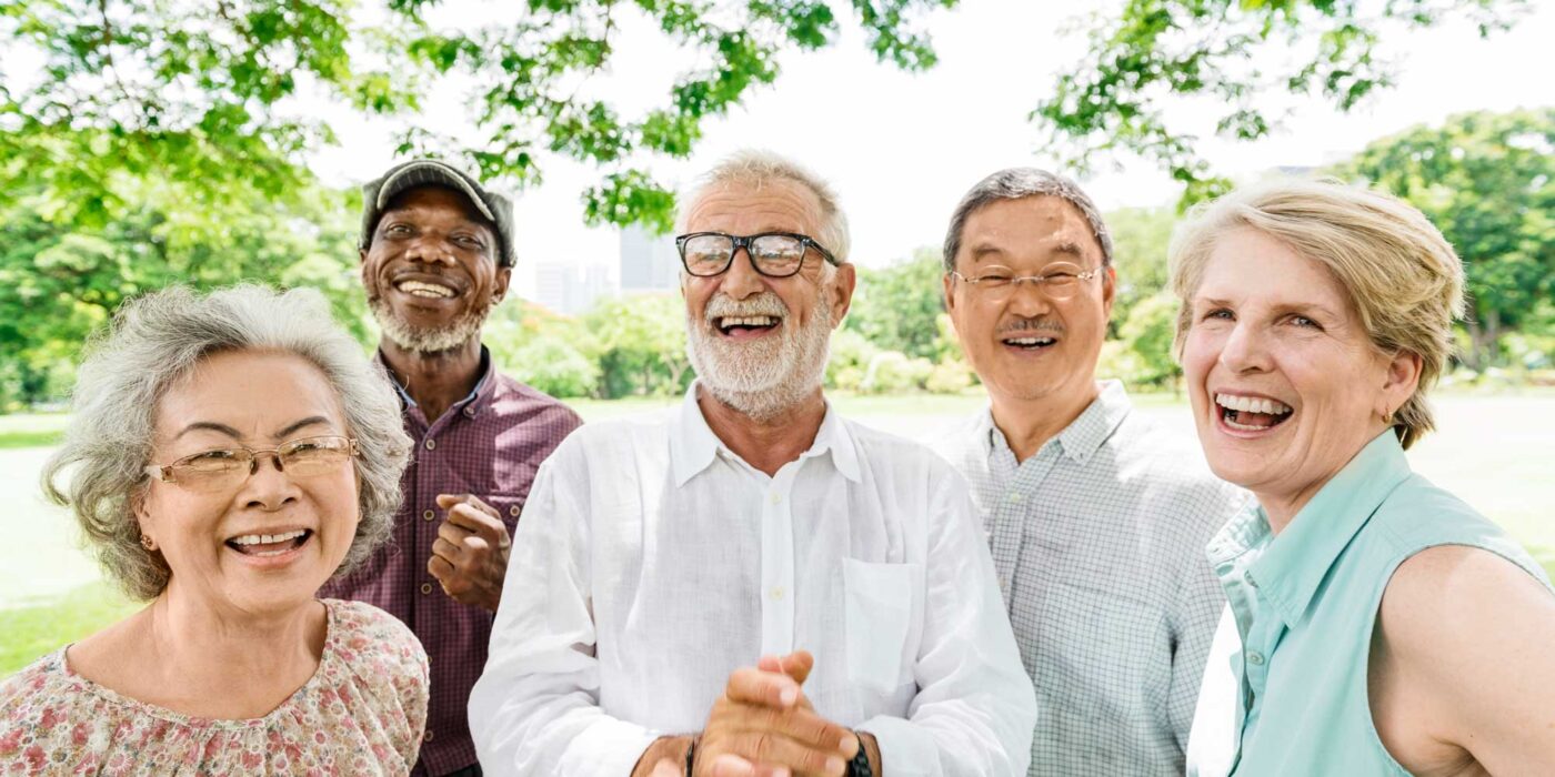 a group of seniors laughing and smiling while outside under the shade of a tree
