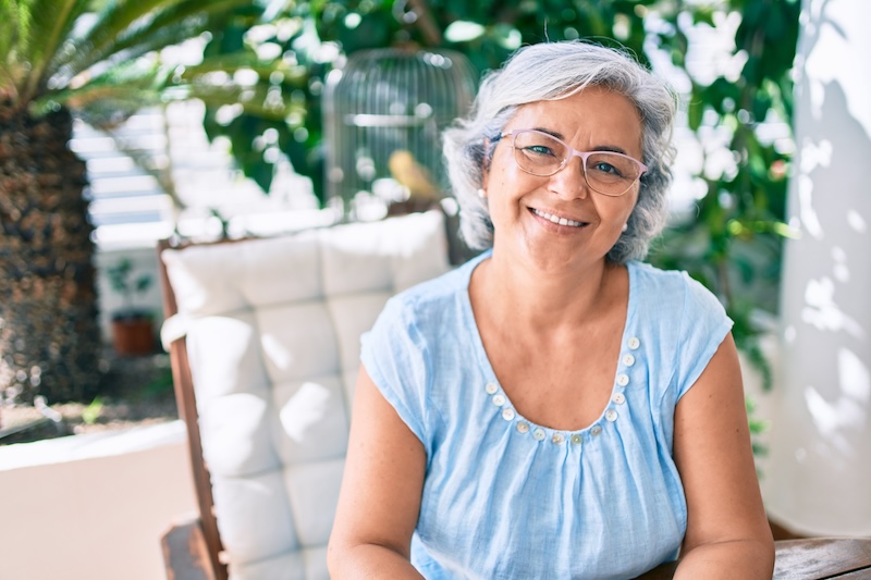 Middle age woman with grey hair smiling happy relaxing sitting at the terrace at home