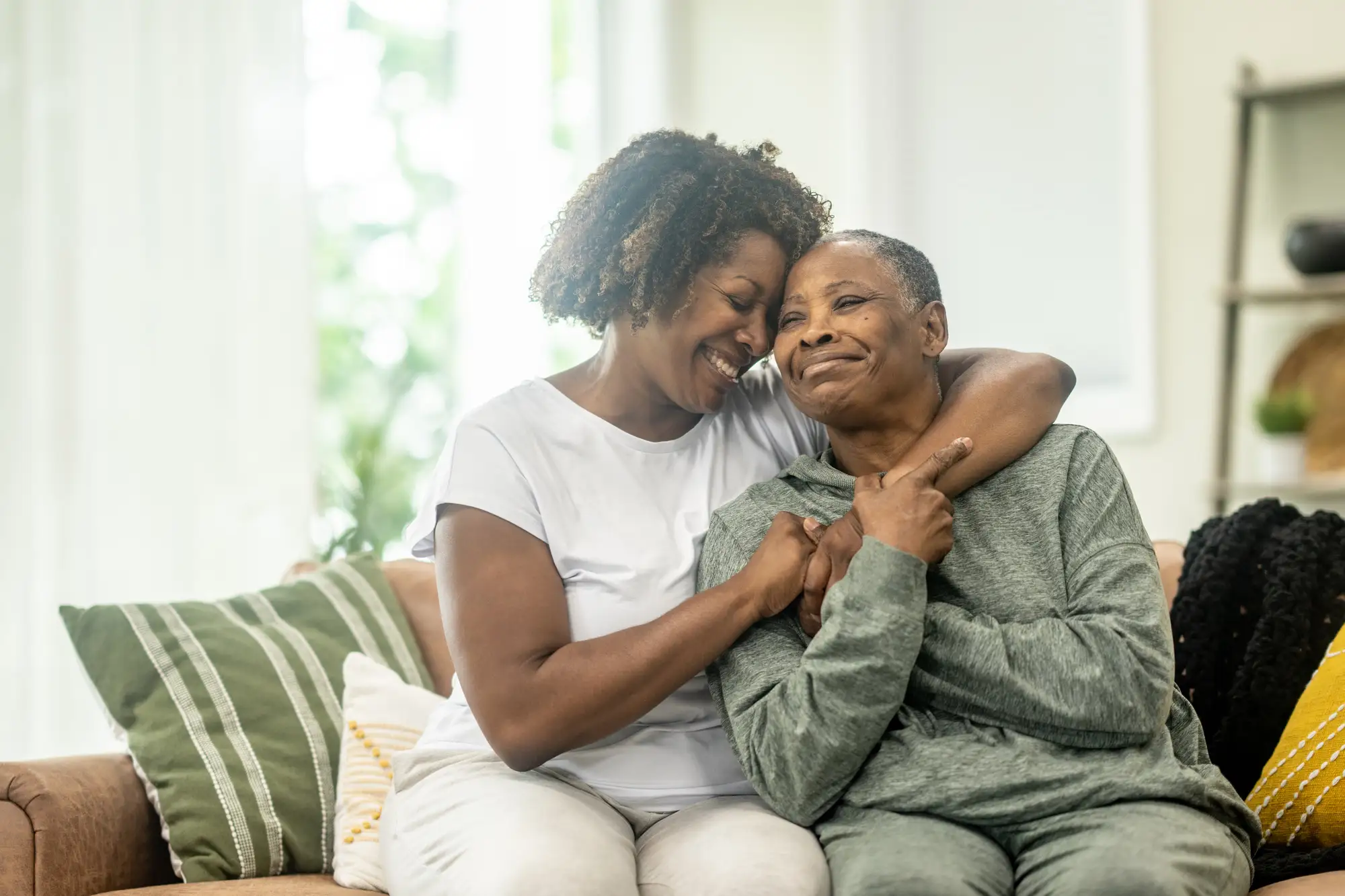 senior woman and adult daughter hug on couch